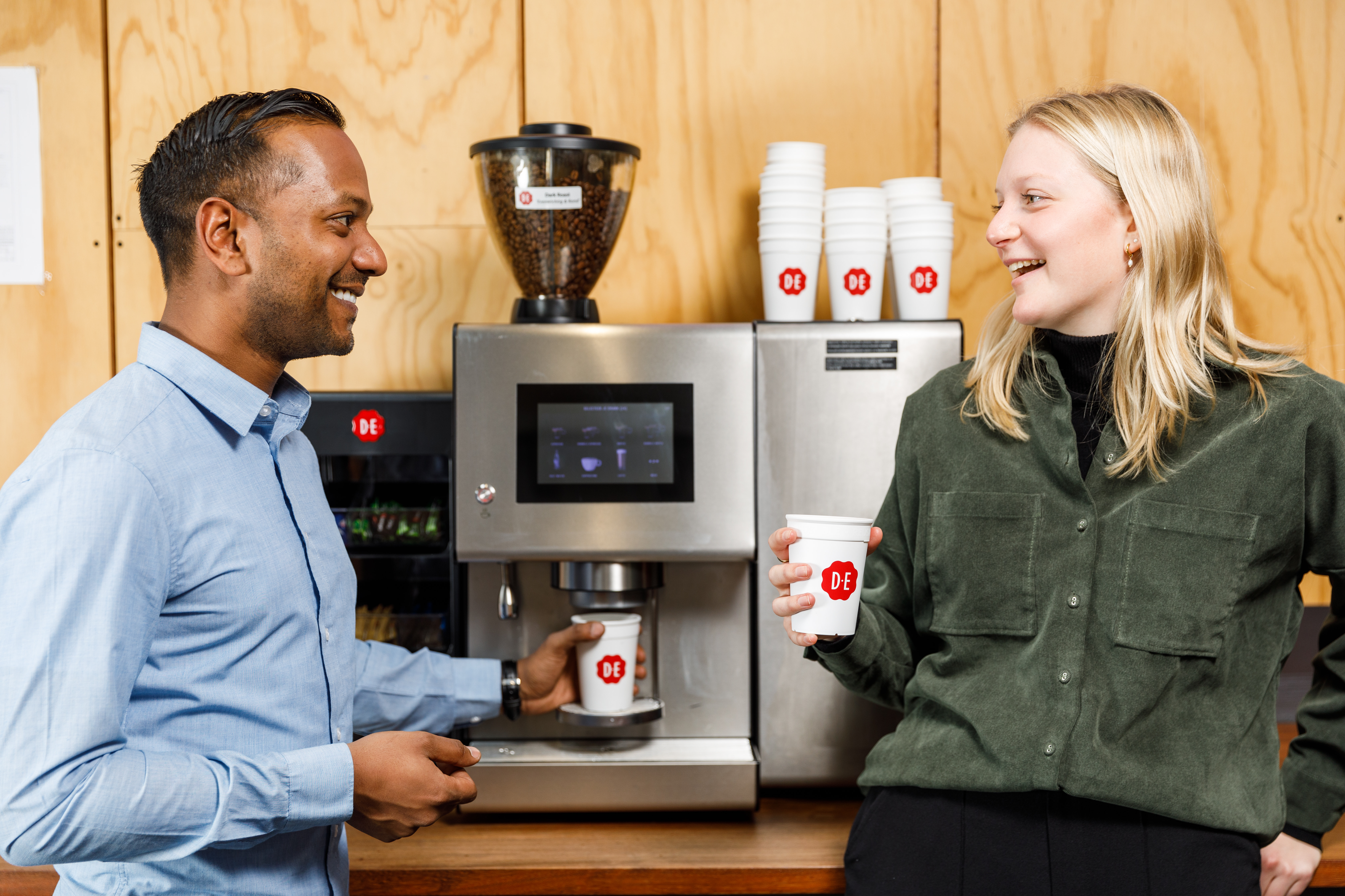 Man en vrouw in gesprek bij een koffiemachine op kantoor