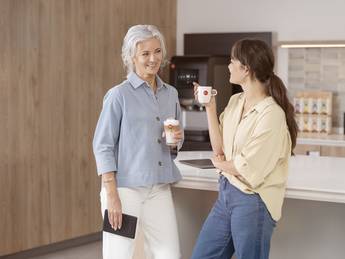 Twee vrouwen met een kopje Douwe Egberts koffie in hun hand met een koffiemachine op de achtergrond