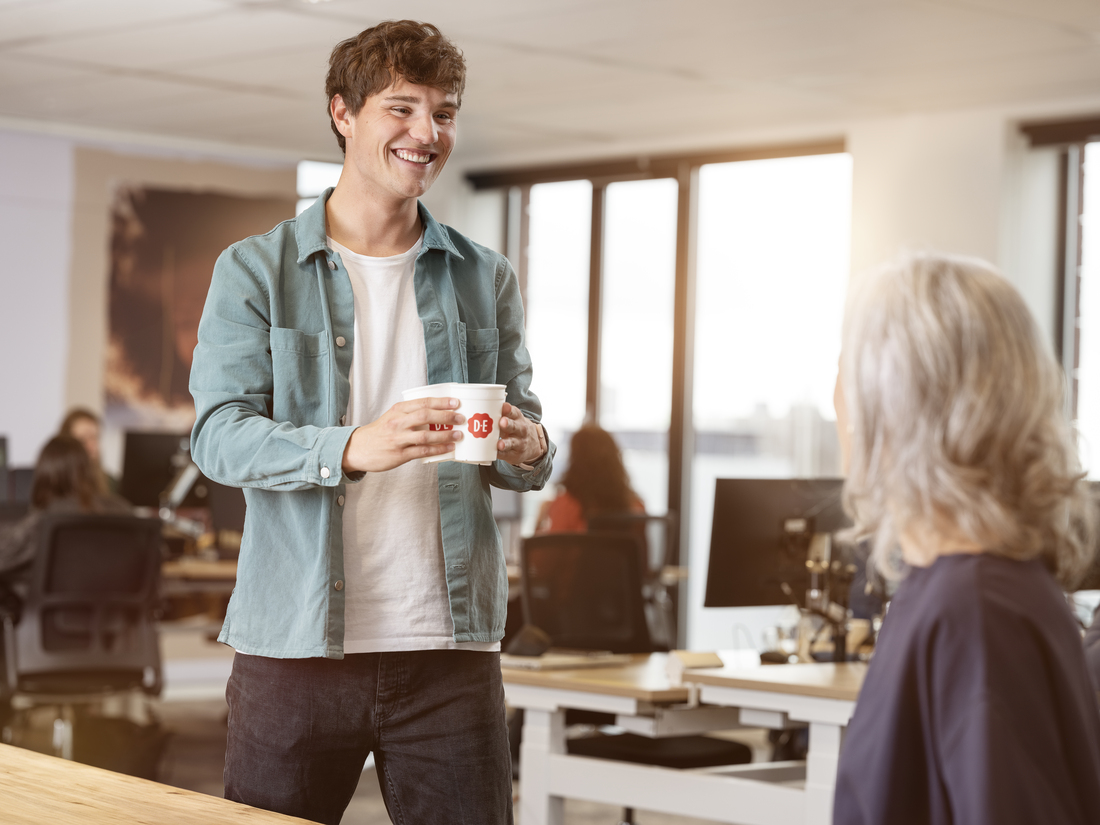 Jongen geeft een kop koffie in een D.E. hard cup aan zijn collega