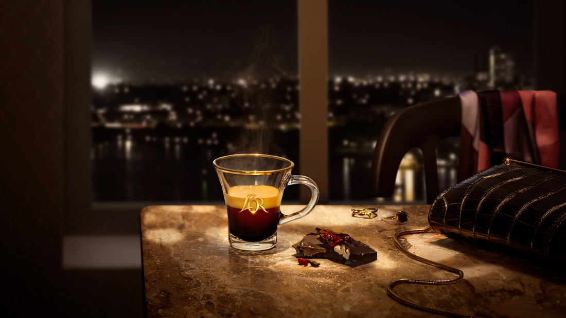 Een glazen L'OR ristretto kopje met een skyline op de achtergrond