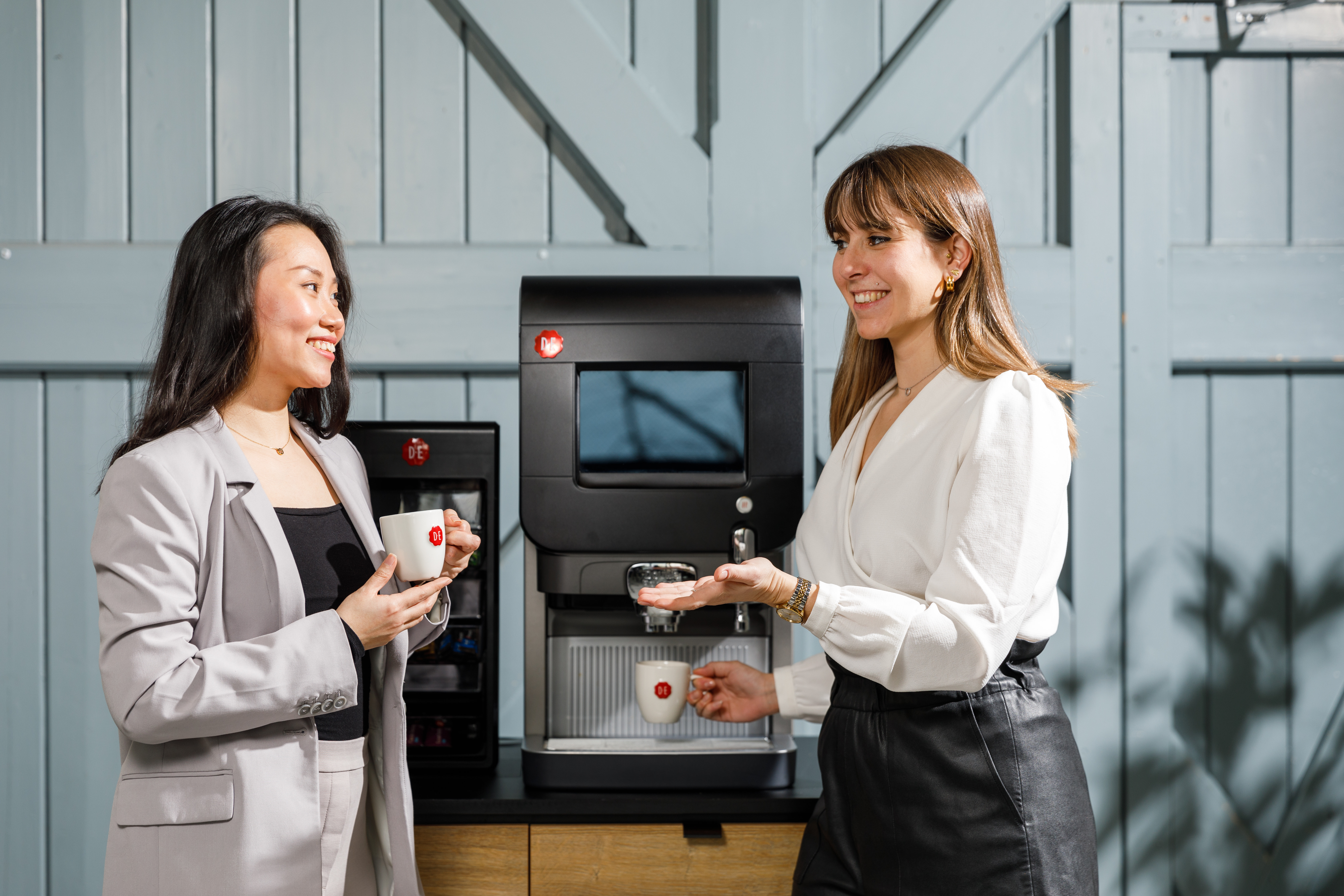 Twee vrouwen in gesprek voor een koffiemachine op werk